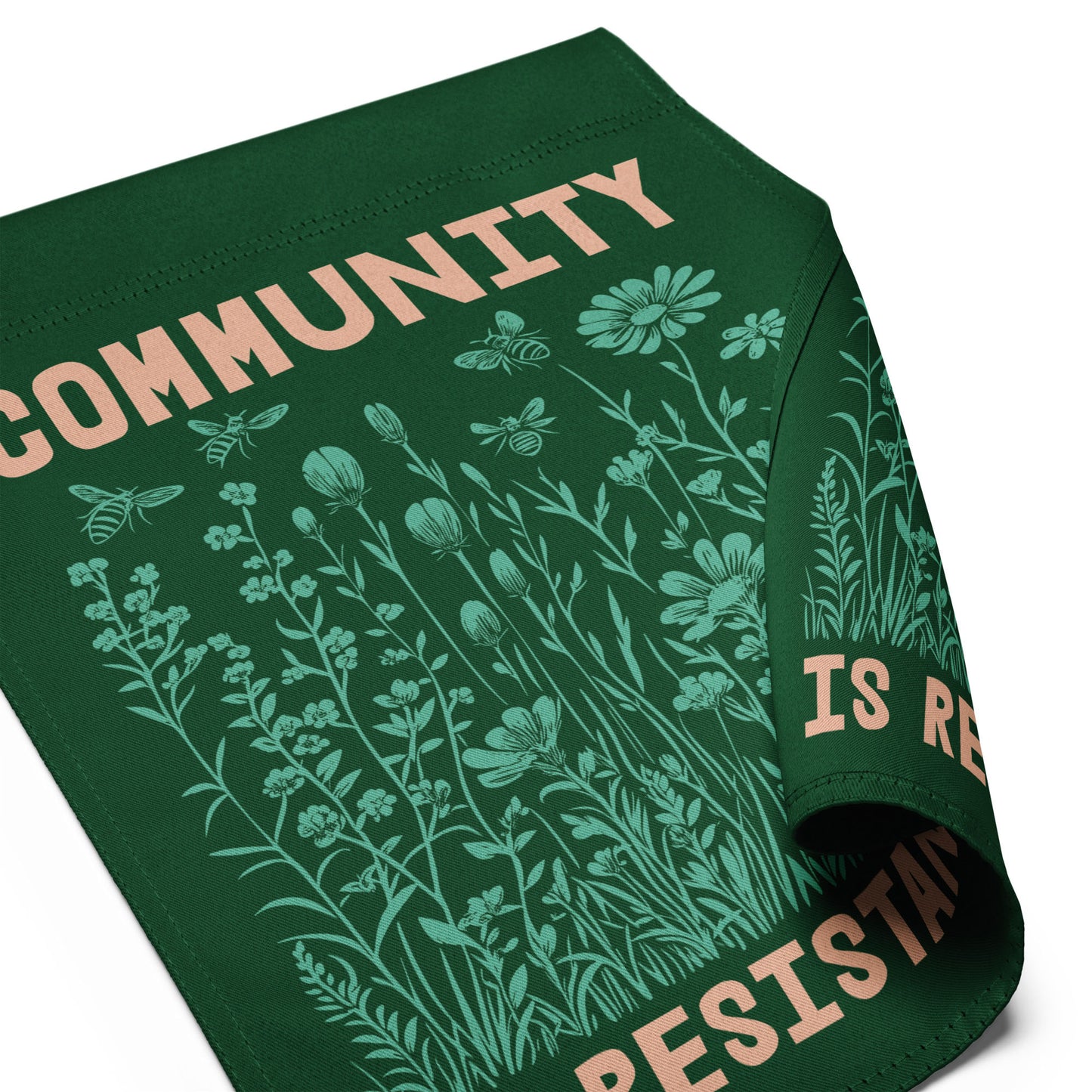 Tight crop of the word “COMMUNITY” printed in cream block letters above fine line botanical illustrations, showing the quality of the print and the message’s quiet strength.