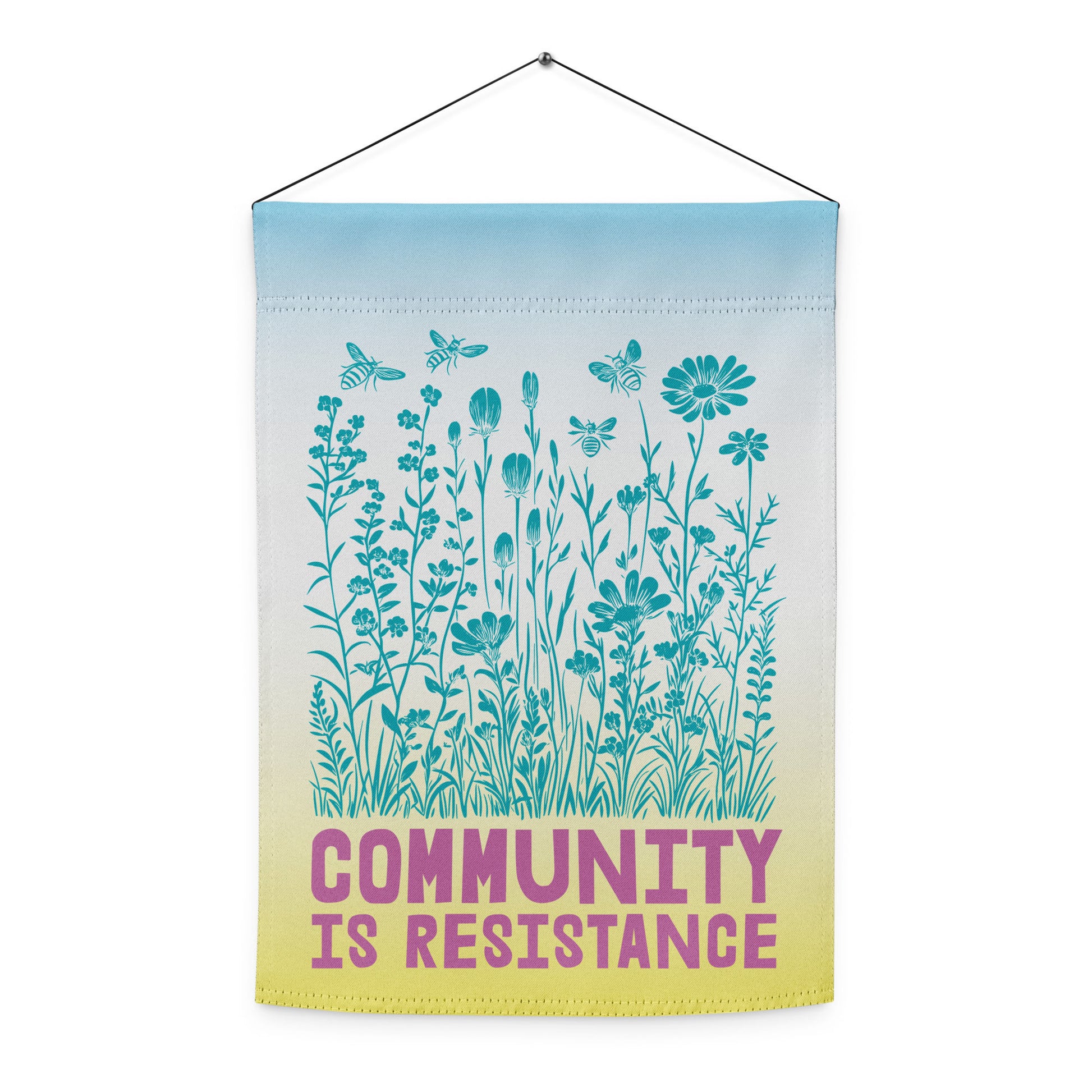 The Community Is Resistance garden flag hung vertically indoors, showing botanical art and warm color gradients — a perfect piece for peaceful, justice-minded homes.