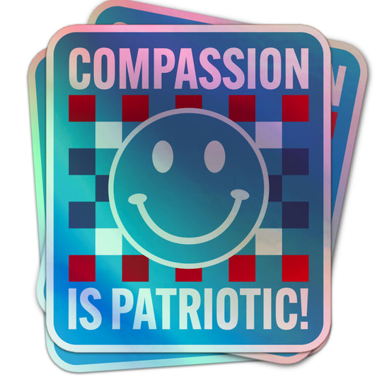 Holographic sticker with a large blue smiley face, blue and red checkerboard pattern, and bold white text reading “Compassion is Patriotic!”