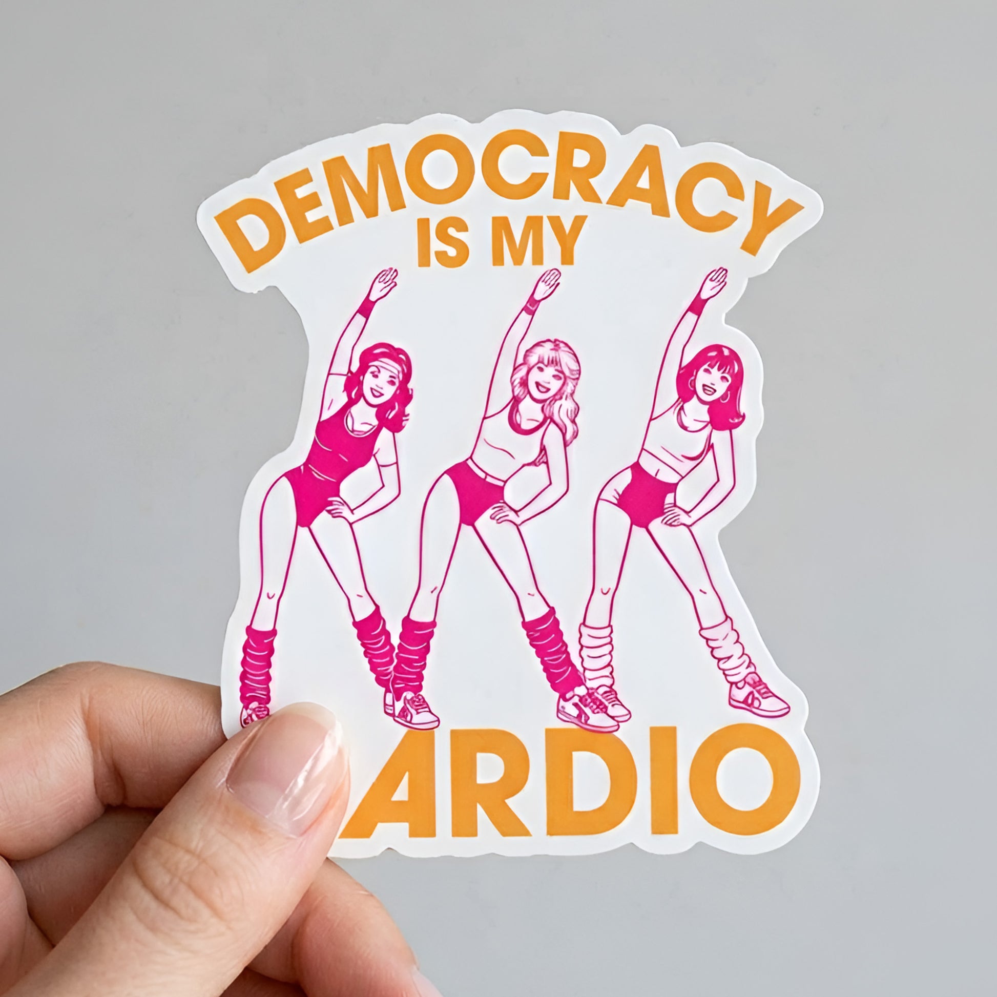 Die-cut sticker featuring retro pink aerobics dancers with bold orange text reading “Democracy Is My Cardio,” playful vintage fitness artwork for activist design and political humor lovers.