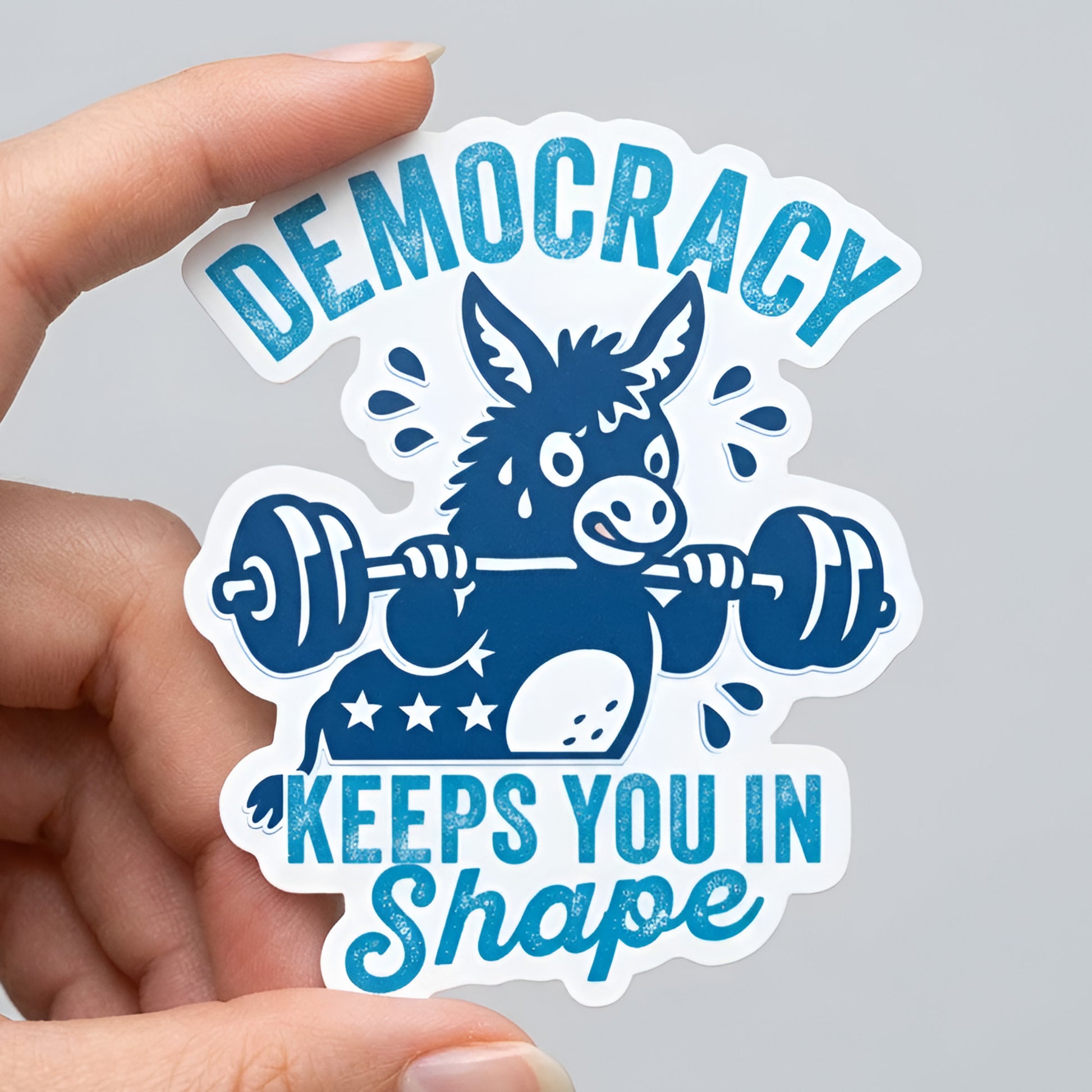 Die-cut sticker featuring a blue donkey lifting a barbell with the phrase “Democracy Keeps You in Shape,” bold fitness-inspired political humor in a justice-focused design style.