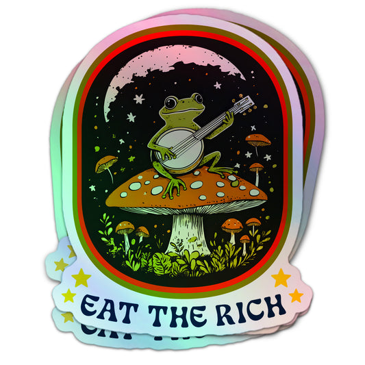 Cottagecore-inspired anti-capitalism holographic sticker with a banjo-playing frog atop a toadstool and protest slogan “Eat The Rich.”