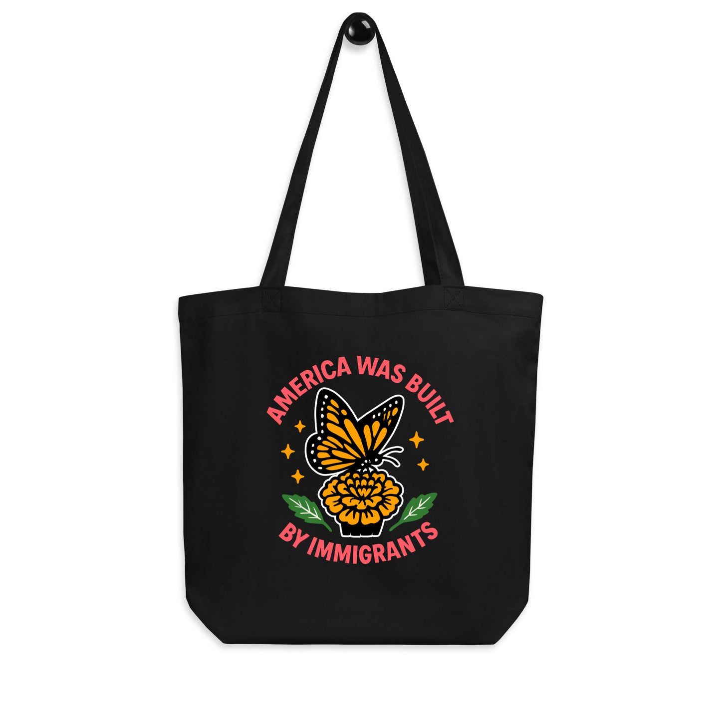 Black “America Was Built by Immigrants” tote bag with monarch butterfly and floral artwork. Activist-inspired design celebrating immigrant heritage.