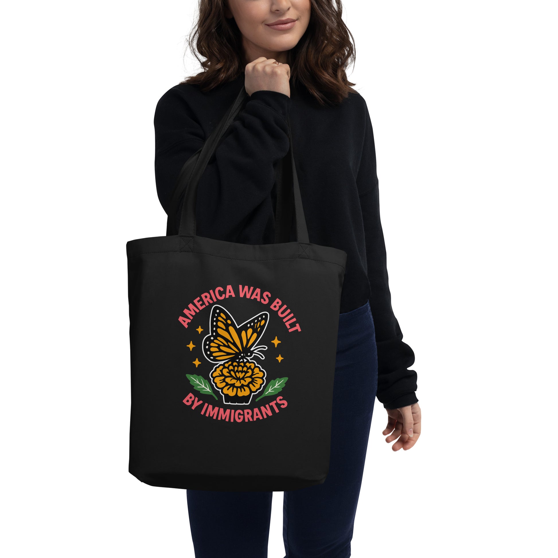 Model wearing black “America Was Built by Immigrants” eco tote bag featuring monarch butterfly and marigold design. Progressive statement bag by Blue Wave USA.