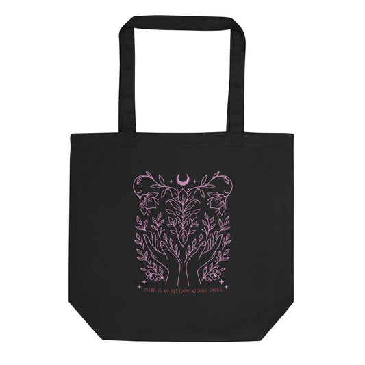 Black eco tote bag featuring a soft pink botanical line art design with hands, vines, and a crescent moon above the phrase “There Is No Freedom Without Choice.”