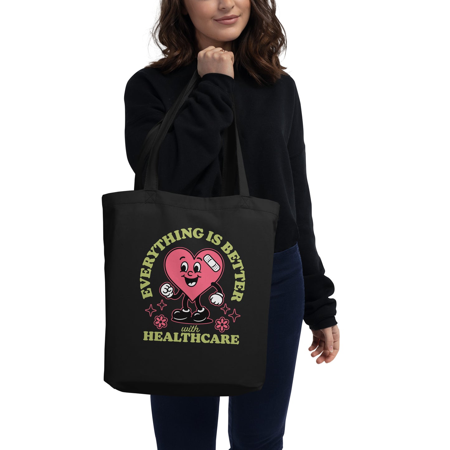 Model holding the “Everything Is Better with Healthcare” black tote bag by the handles, showing full heart design and message supporting universal healthcare.