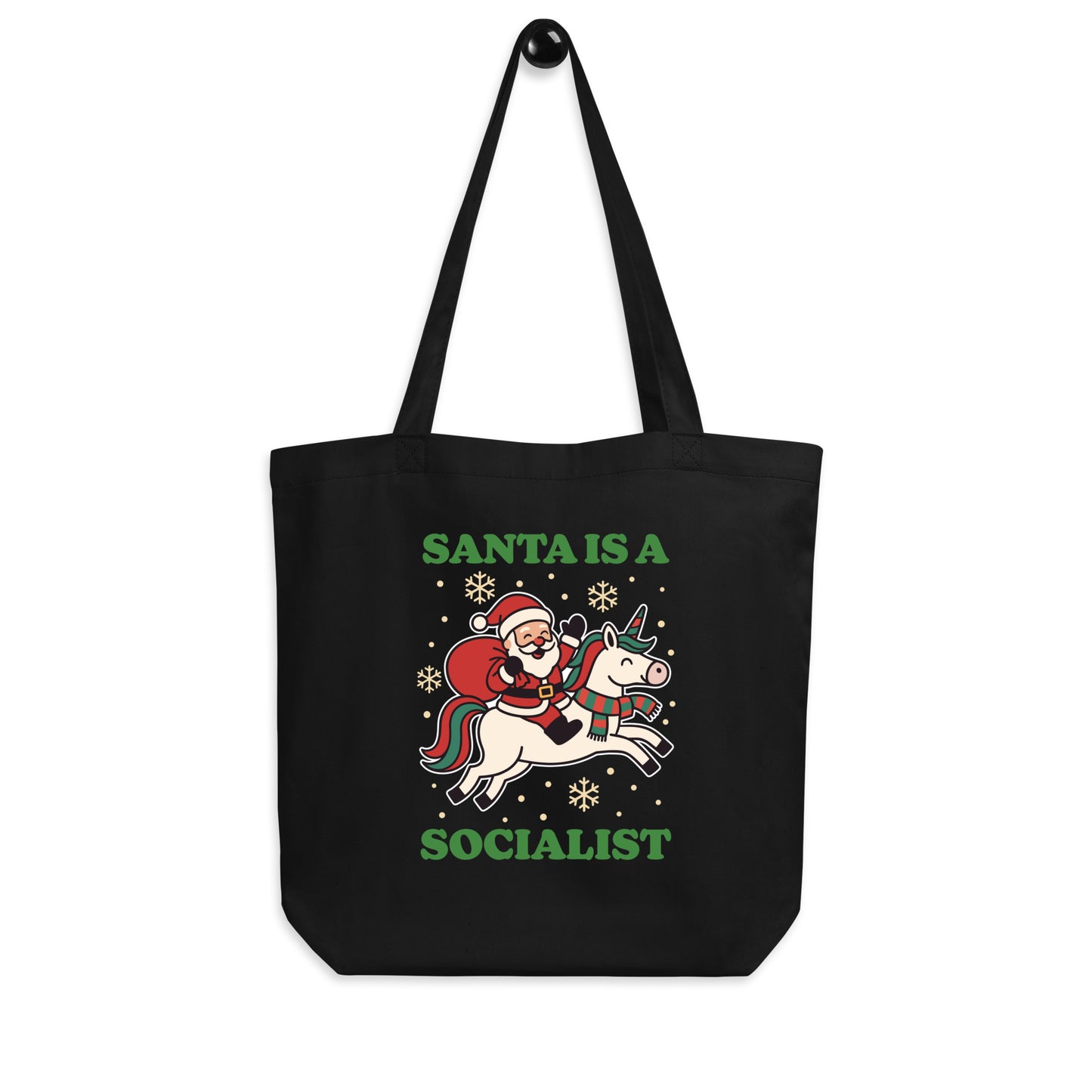 Black tote bag hanging on a hook, printed with a vintage-style Santa riding a unicorn illustration, holiday stars, and the message “SANTA IS A SOCIALIST,” from Blue Wave USA.