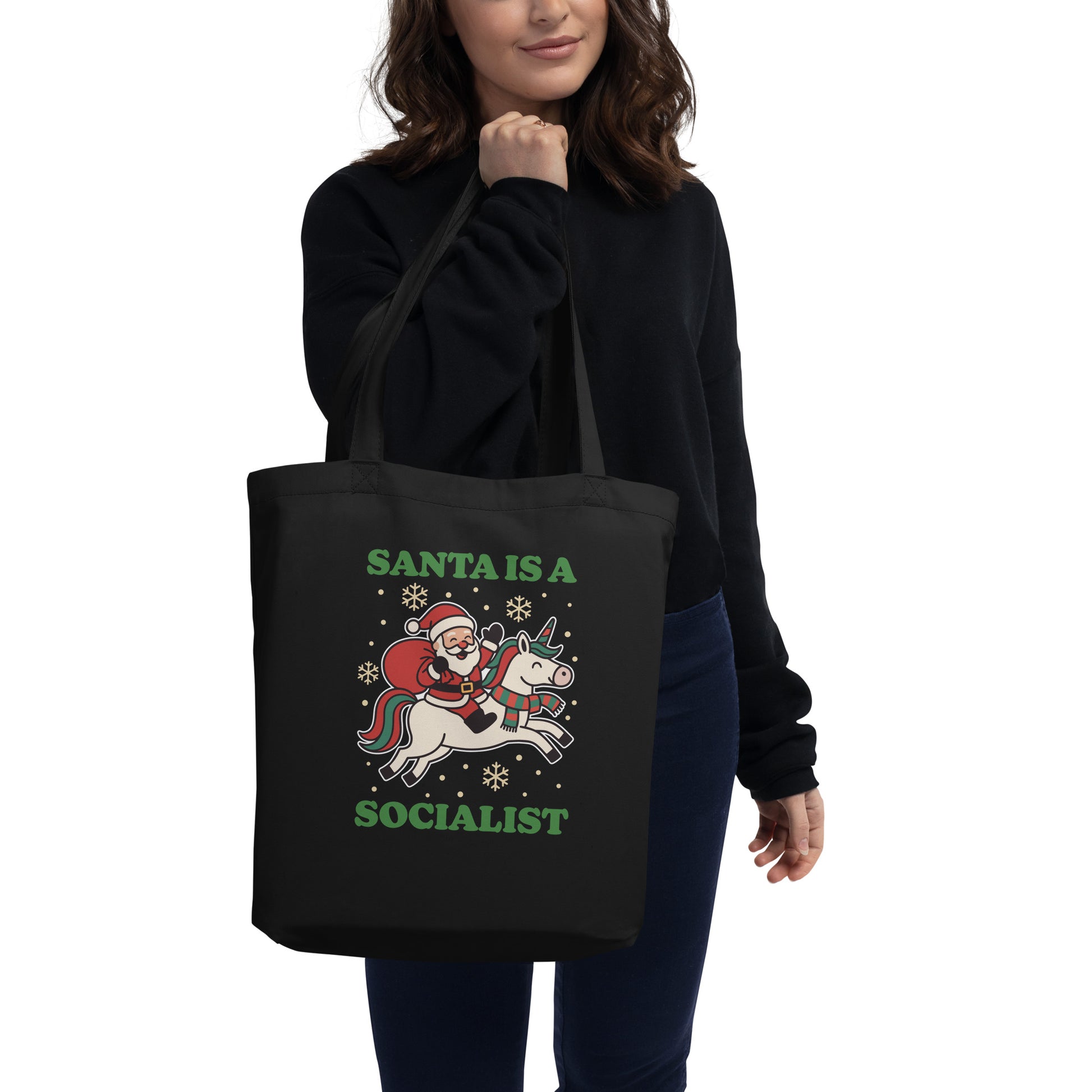 Model carrying a black tote bag featuring a vintage Santa riding a unicorn with holiday stars and the printed message “SANTA IS A SOCIALIST,” designed by Blue Wave USA.