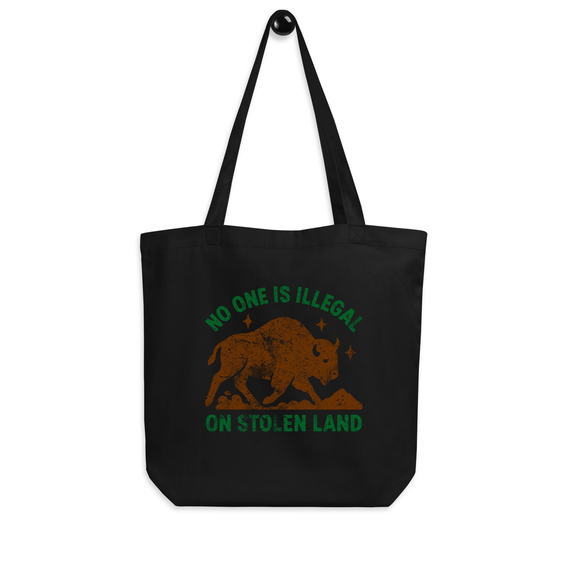 Black canvas tote bag with the distressed buffalo graphic and the text “NO ONE IS ILLEGAL ON STOLEN LAND,” combining earthy print tones with an anti-colonial message.
