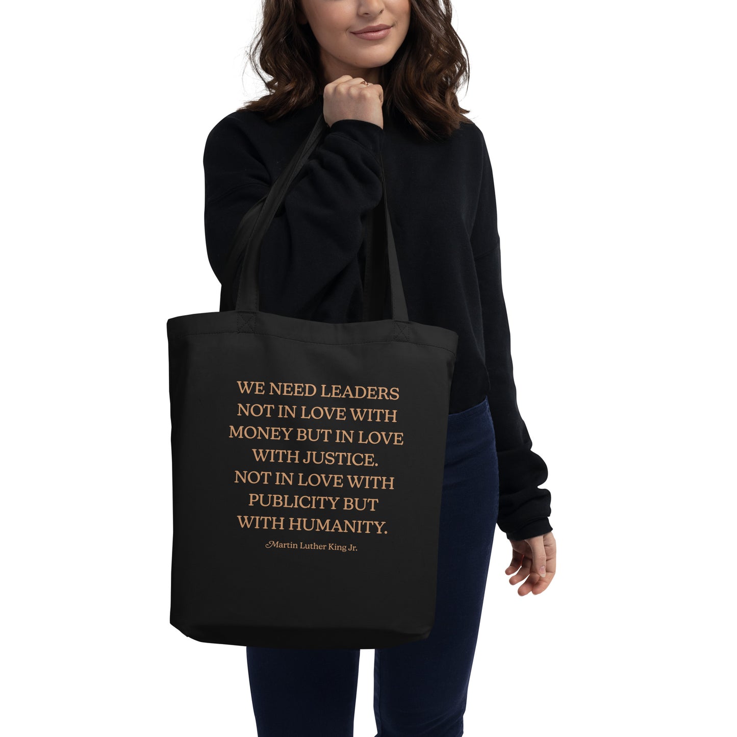 Model carrying a black eco tote bag featuring the MLK quote calling for leaders who choose justice and humanity over money and publicity. A thoughtful activist accessory.