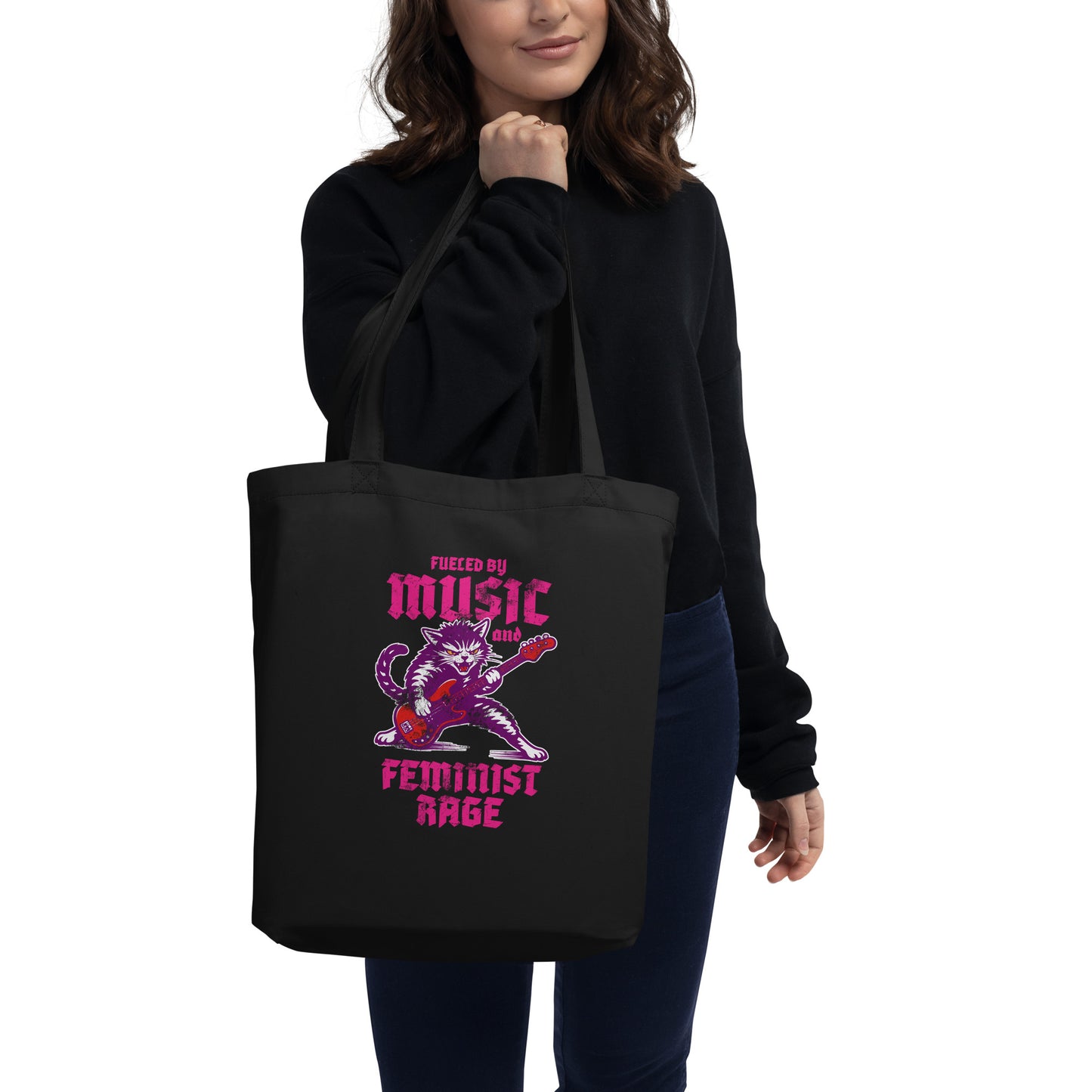Model wearing a black eco tote bag over the shoulder, featuring the punk rock cat electric guitar illustration and the phrase “FUELED BY MUSIC AND FEMINIST RAGE,” casual lifestyle setting from Blue Wave USA.