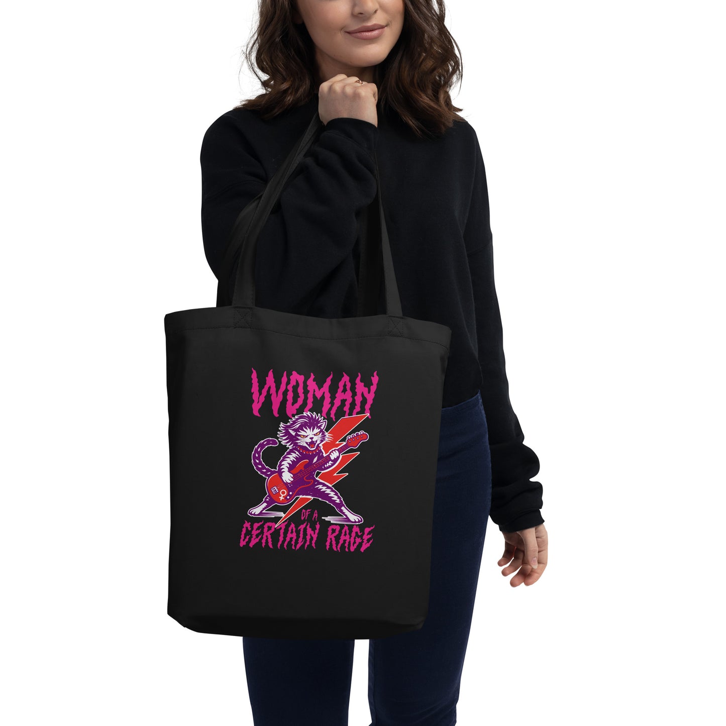 Model wearing a black eco tote bag over the shoulder, featuring the punk rock cat electric guitar illustration and distressed lettering reading “WOMAN OF A CERTAIN RAGE,” casual lifestyle setting from Blue Wave USA.