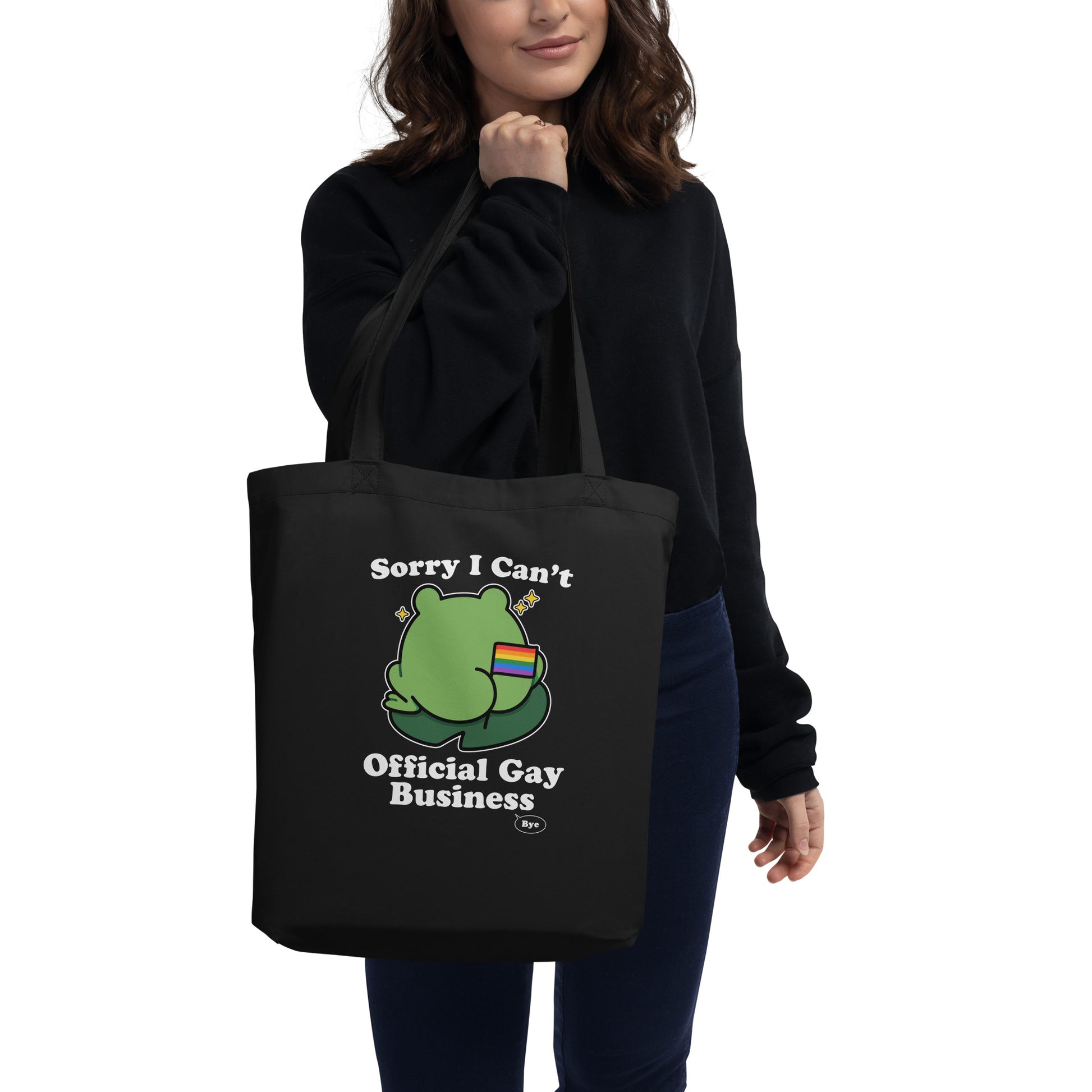 Person carrying a black tote bag featuring a frog holding a rainbow flag with playful “Sorry I Can’t. Official Gay Business. Bye.” design.