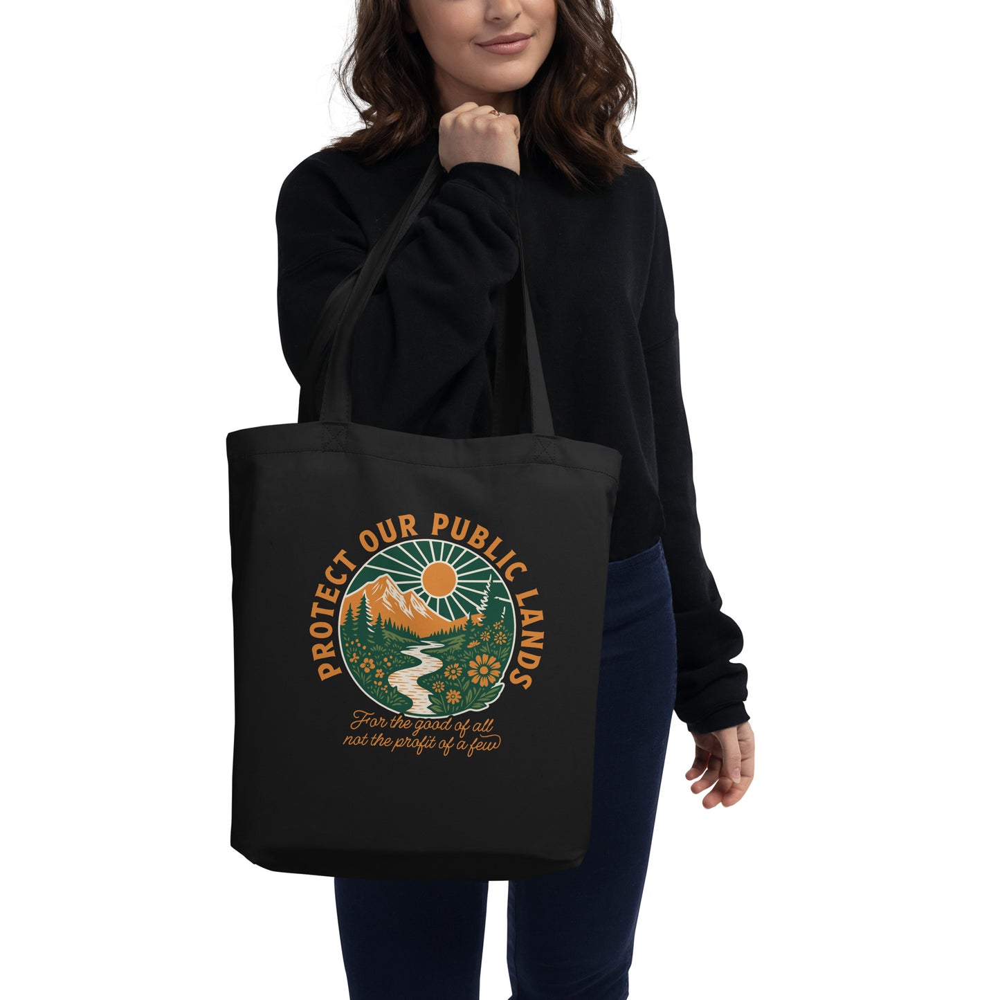 Person carrying a black eco tote bag featuring “Protect Our Public Lands” artwork inspired by national parks, conservation, and environmental advocacy.