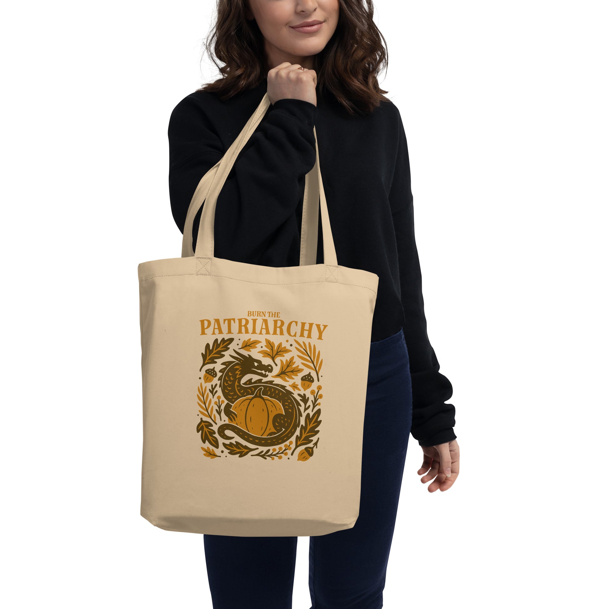 Model carrying the natural “Burn the Patriarchy” eco tote bag with dragon and pumpkin design in warm autumn colors. Progressive feminist Thanksgiving tote by Blue Wave USA.