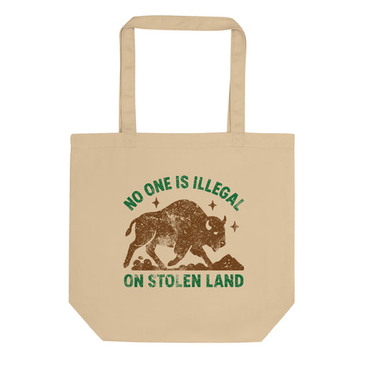Beige canvas tote bag featuring an earthy buffalo illustration with stars and the message “NO ONE IS ILLEGAL ON STOLEN LAND,” printed in rustic brown and green tones.
