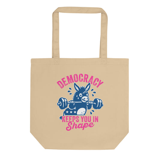 Eco tote bag featuring a blue donkey lifting a barbell with pink “Democracy Keeps You in Shape” text, fitness-inspired political humor artwork for everyday progressive accessories.