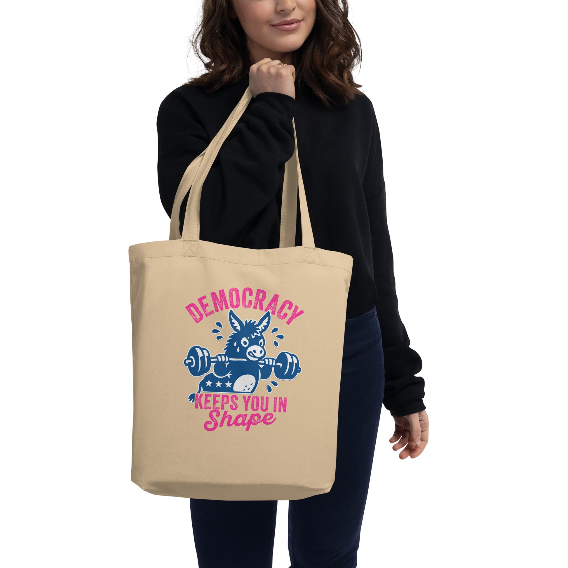 Blue Wave USA eco tote carried on shoulder, showing donkey weightlifting graphic with democracy workout slogan in playful justice-focused design styling.