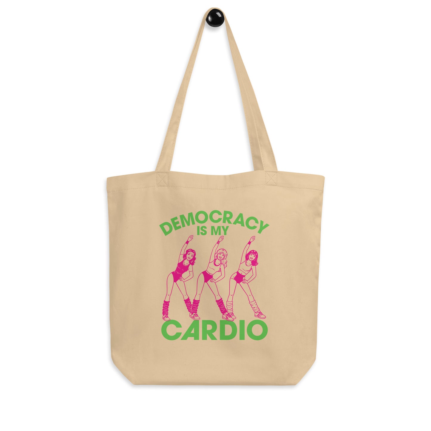 Natural canvas tote displaying pink retro workout dancers and democracy cardio phrase in green lettering, civic humor accessory for books, errands, and market trips.