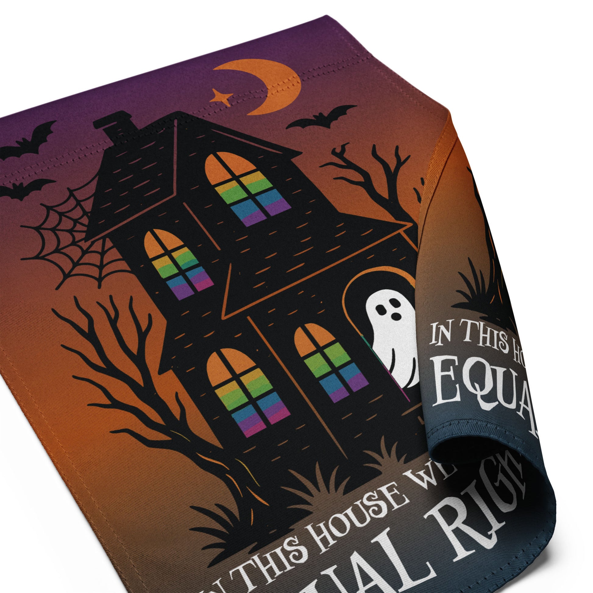 Close-up of the “In This House We Believe in Equal Rights” haunted house Halloween flag with curled edge showing rainbow windows and spooky details.
