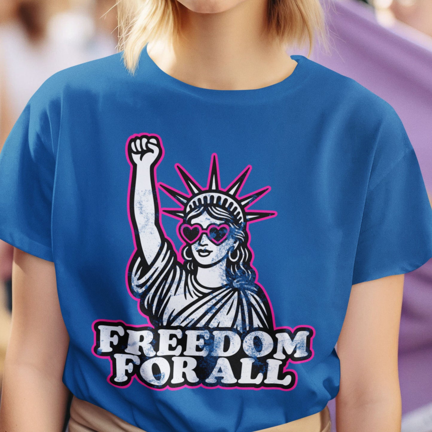 Model wearing royal blue unisex t-shirt featuring Statue of Liberty raised fist graphic with bold text reading “FREEDOM FOR ALL,” casual street styling.