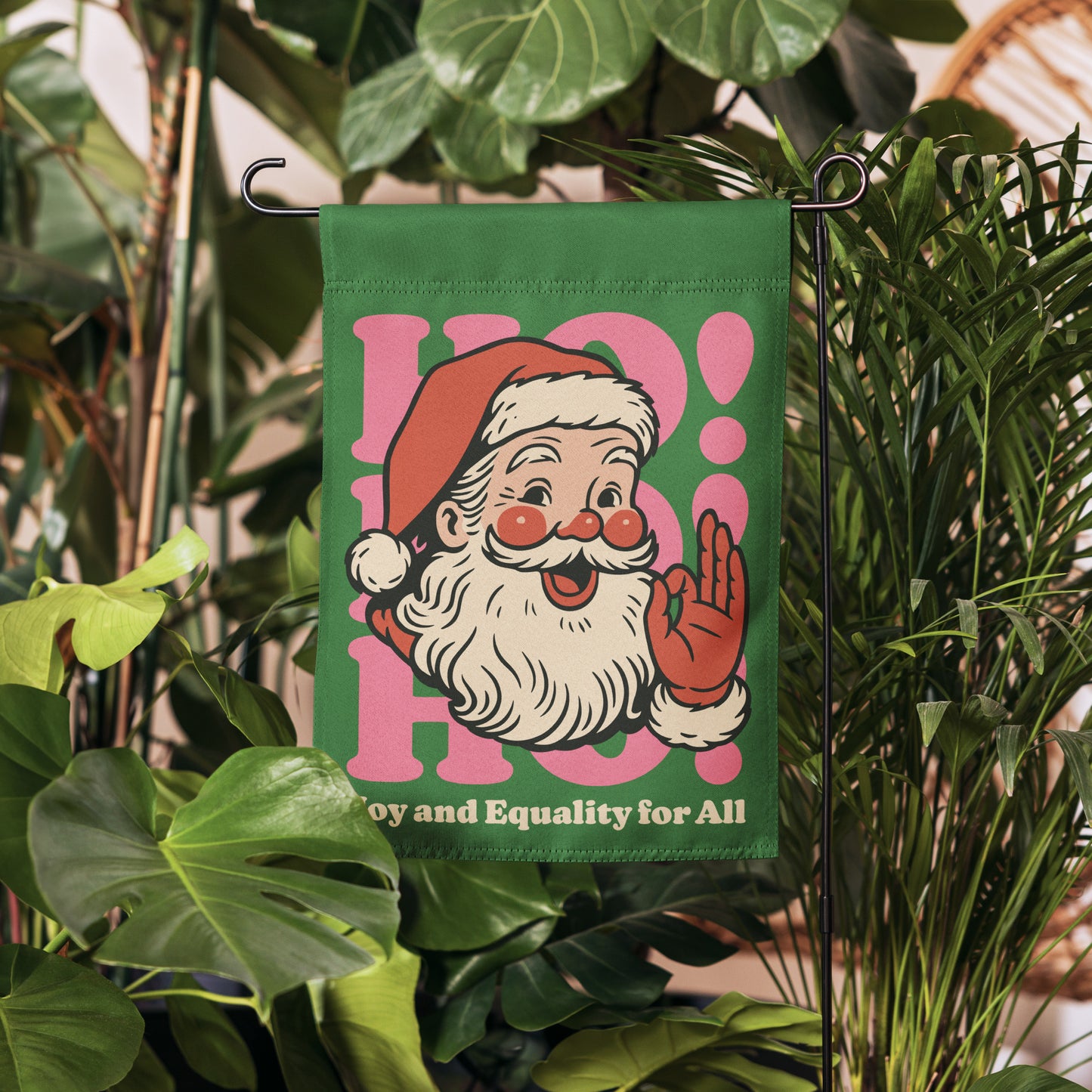 Retro Santa garden flag displayed among lush green plants, showcasing the pink mid-century graphic accents and equality message from Blue Wave USA.