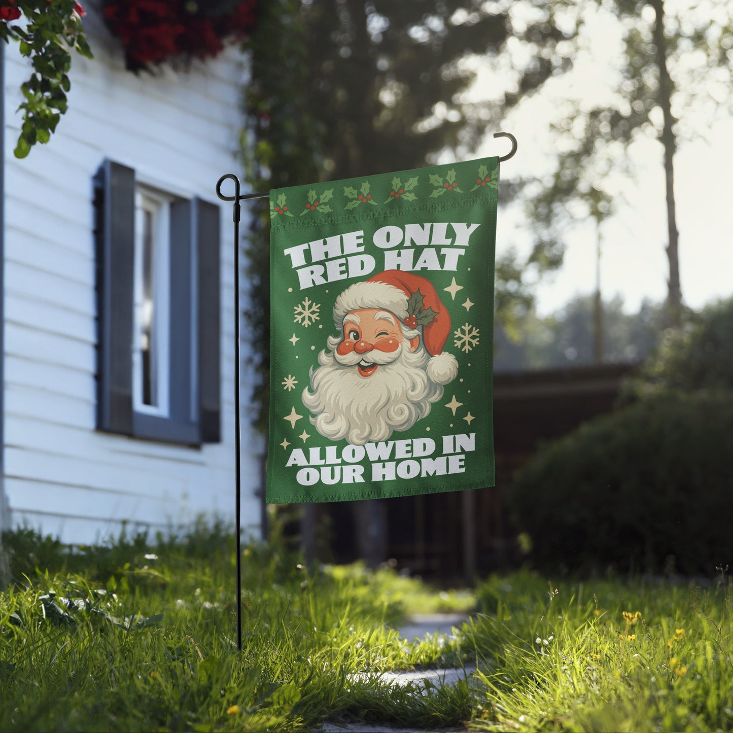 Green garden flag displayed outside a home, featuring a vintage-style Santa graphic, snowflakes, holly accents, and the message “THE ONLY RED HAT ALLOWED IN OUR HOME.”
