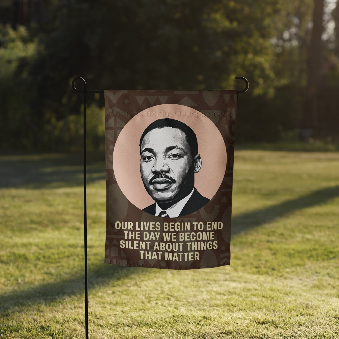 Garden flag featuring MLK’s portrait and the text “OUR LIVES BEGIN TO END THE DAY WE BECOME SILENT ABOUT THINGS THAT MATTER,” standing in a shaded grassy yard. Blue Wave USA design.