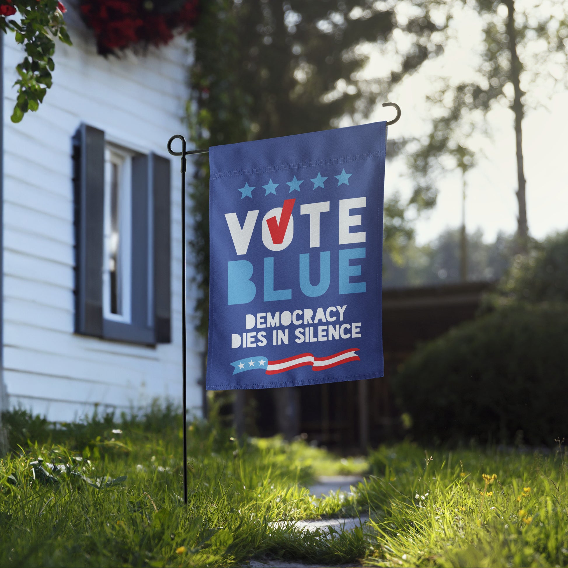Side view of a blue Democratic campaign garden flag placed near a white house walkway, showing the flag's scale in a residential setting.