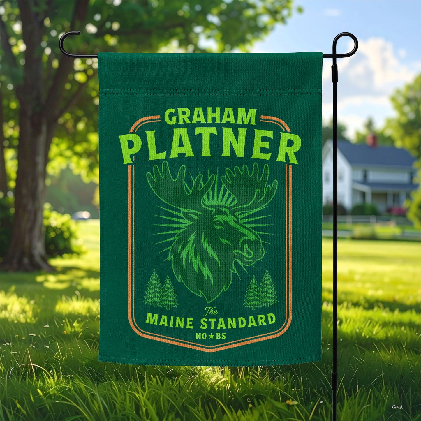 Green garden flag with moose graphic and “Graham Platner Maine Standard” text displayed outdoors on lawn with trees and suburban home background.