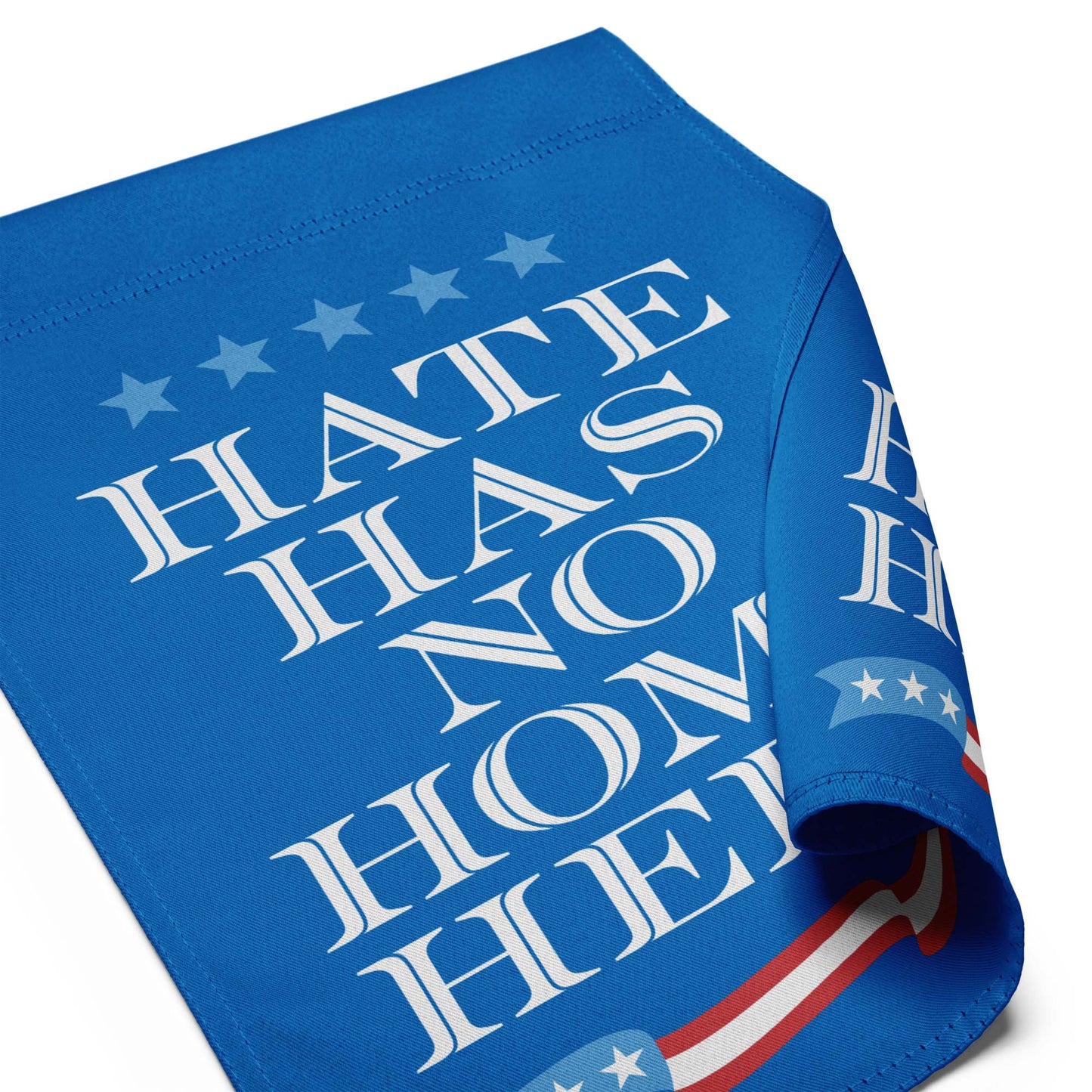 Folded blue garden flag revealing repeated white text “HATE HAS NO HOME HERE,” durable fabric texture and crisp print alignment.