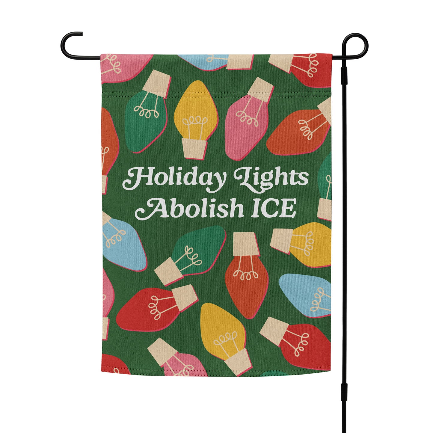 A green garden flag decorated with bright illustrated holiday bulbs surrounding the message “Holiday Lights Abolish ICE,” displayed on a simple outdoor pole to highlight the design.