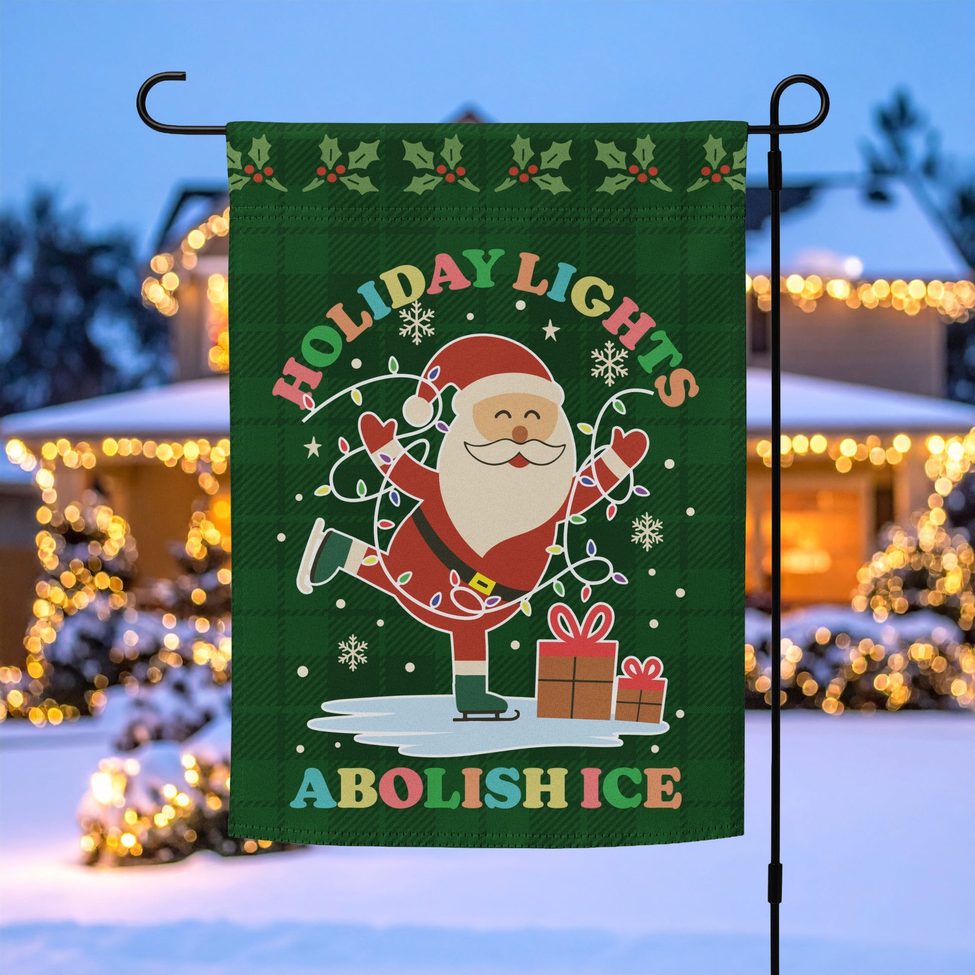 A green garden flag featuring Santa with holiday lights, stars, and wrapped gifts around the message “HOLIDAY LIGHTS ABOLISH ICE,” displayed outdoors in a snowy festive yard for progressive Christmas decor.