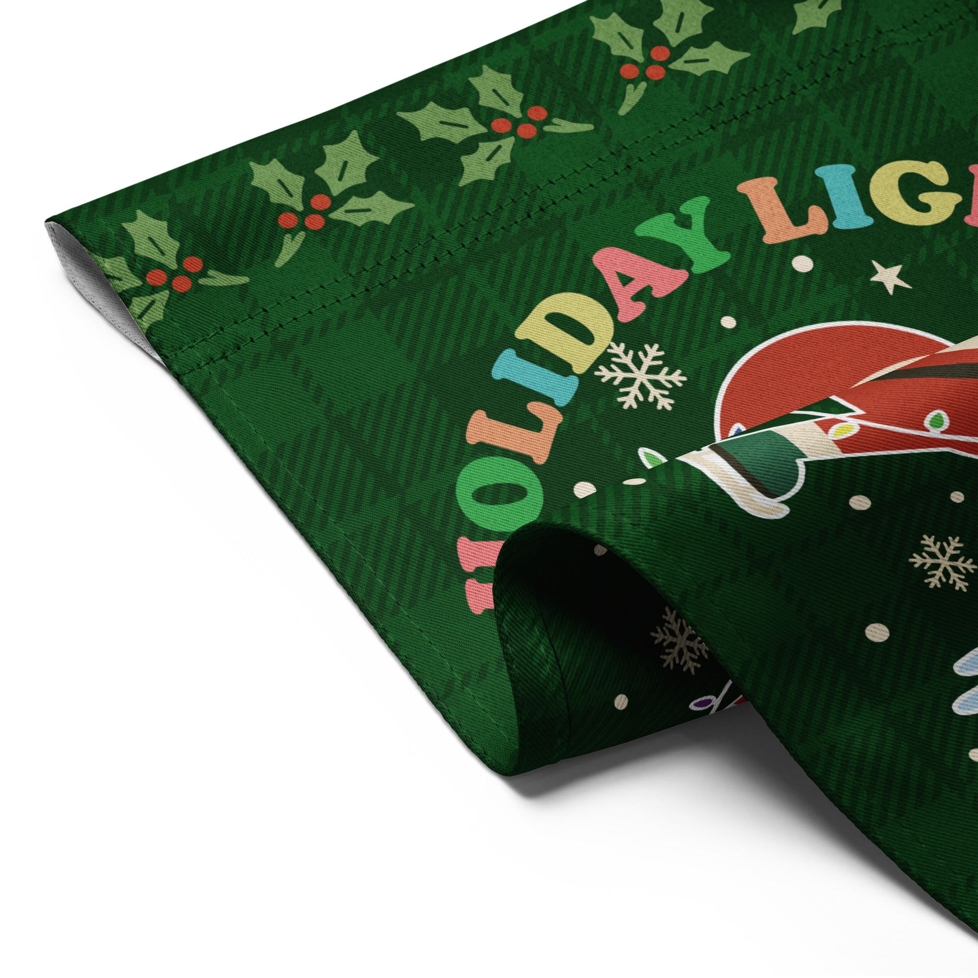 A close-up of a folded green garden flag showing Santa, colorful holiday lights, stars, and accents beside the message “HOLIDAY LIGHTS ABOLISH ICE,” highlighting durable printed fabric from Blue Wave USA.