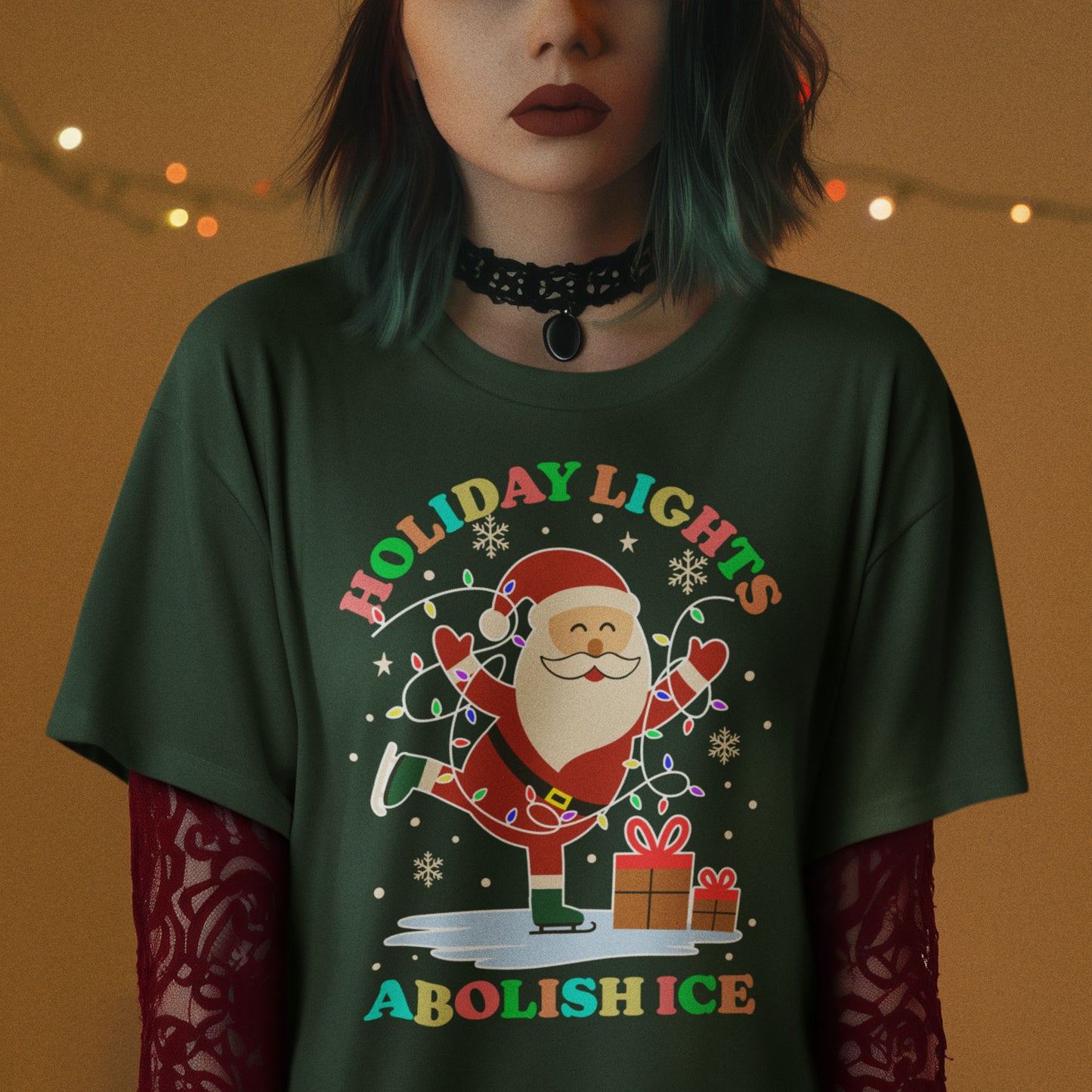 Person wearing a forest green t-shirt featuring Santa with gifts and lights, printed with “HOLIDAY LIGHTS ABOLISH ICE,” shown in warm indoor holiday lighting.