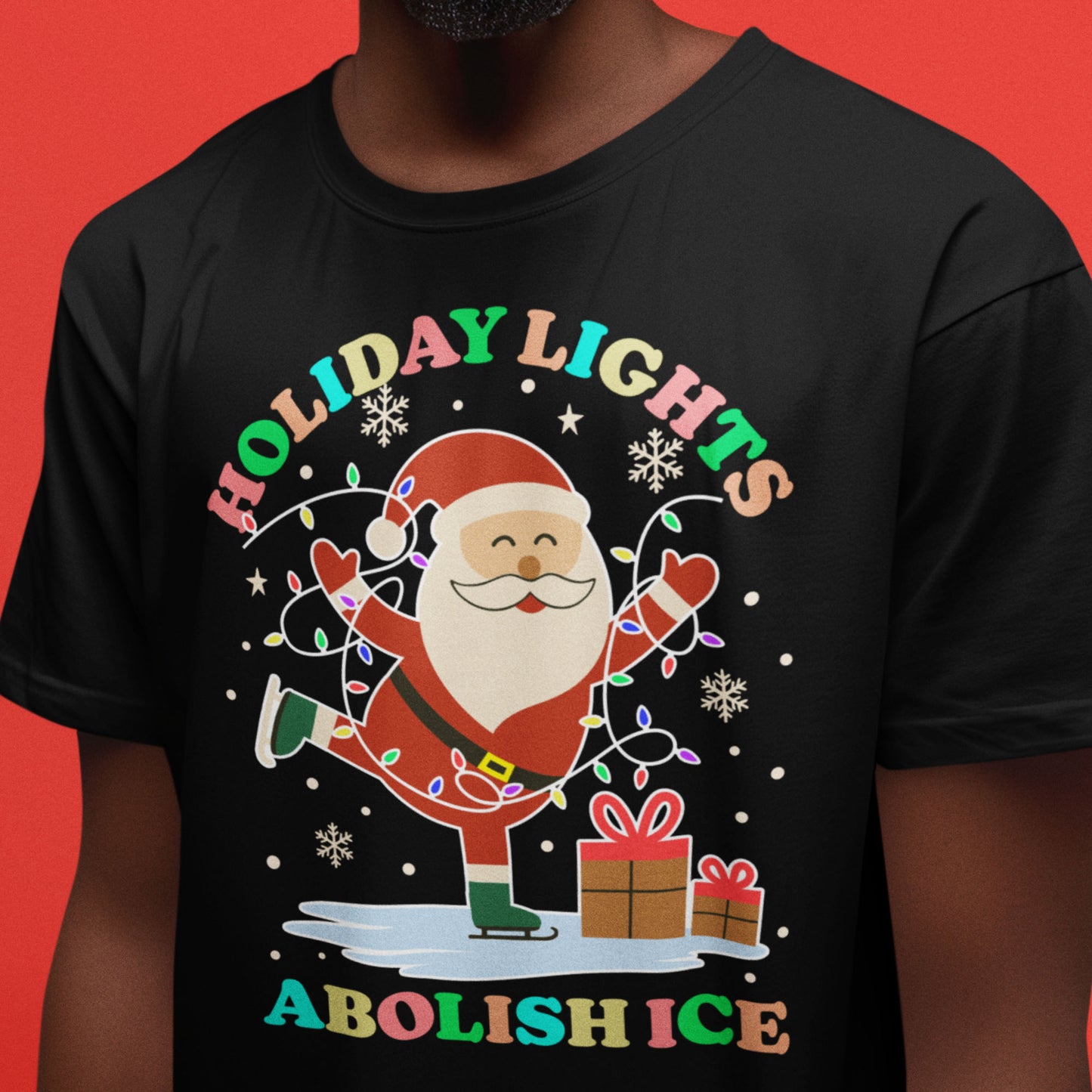 Model wearing a black t-shirt with a cheerful Santa, presents, and holiday lights surrounding the phrase “HOLIDAY LIGHTS ABOLISH ICE,” progressive Christmas design by Blue Wave USA.