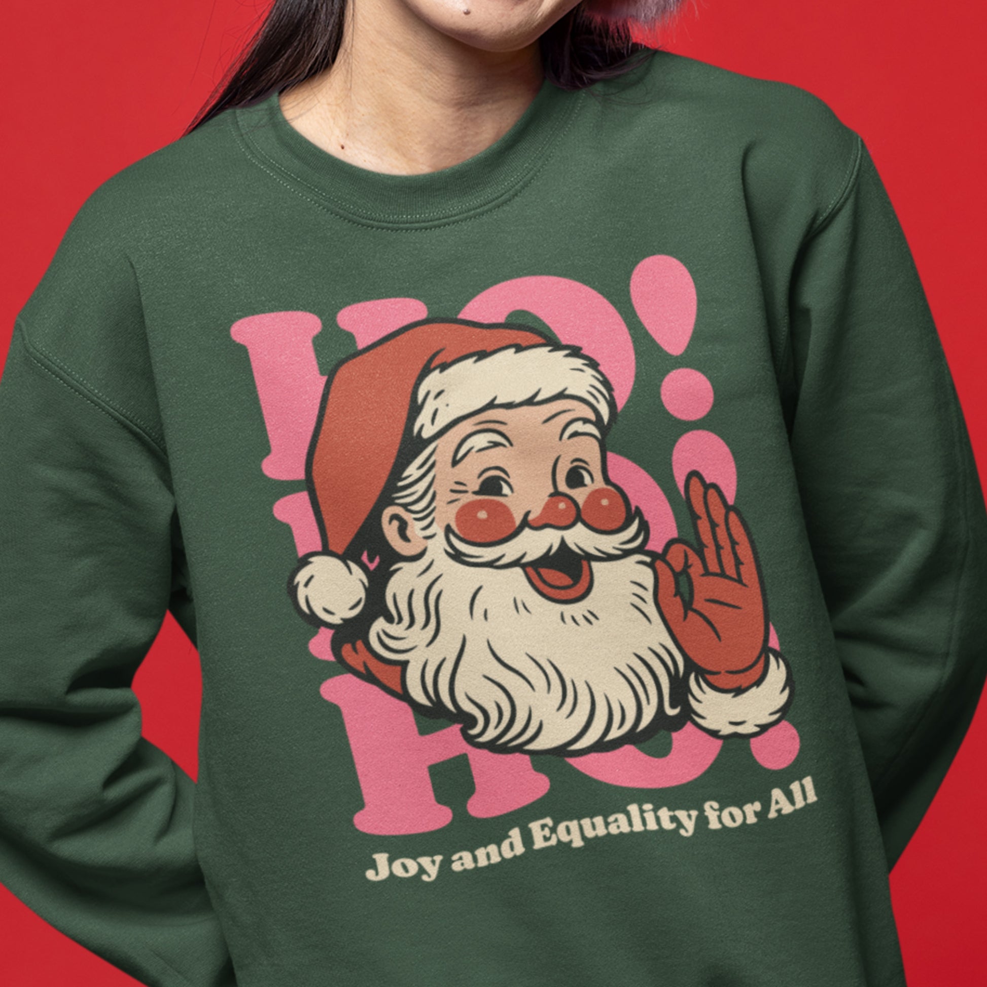 A person wearing the green crewneck with the vintage Santa graphic and inclusive “Joy and Equality for All” message, styled in a festive setting.
