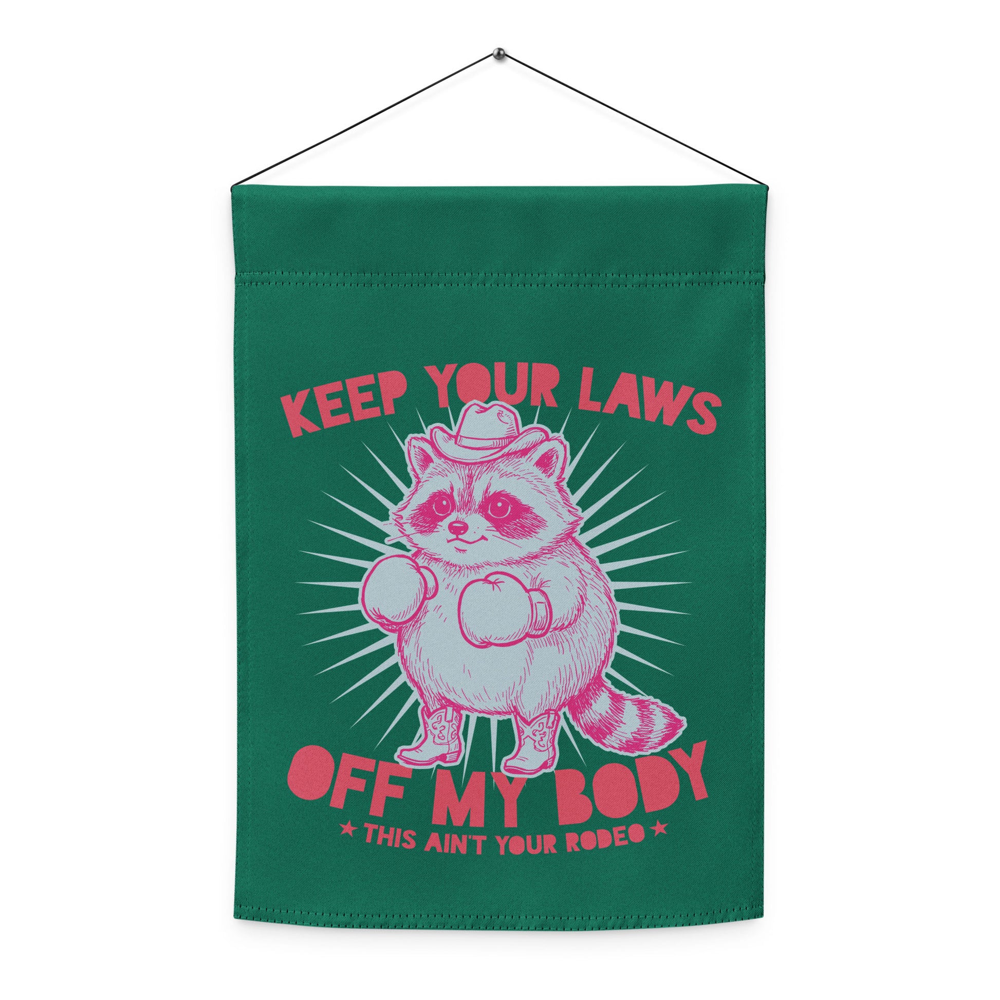 Hanging green garden flag displaying pink raccoon cowboy artwork with “Keep Your Laws Off My Body” phrase in bold feminist activist design.