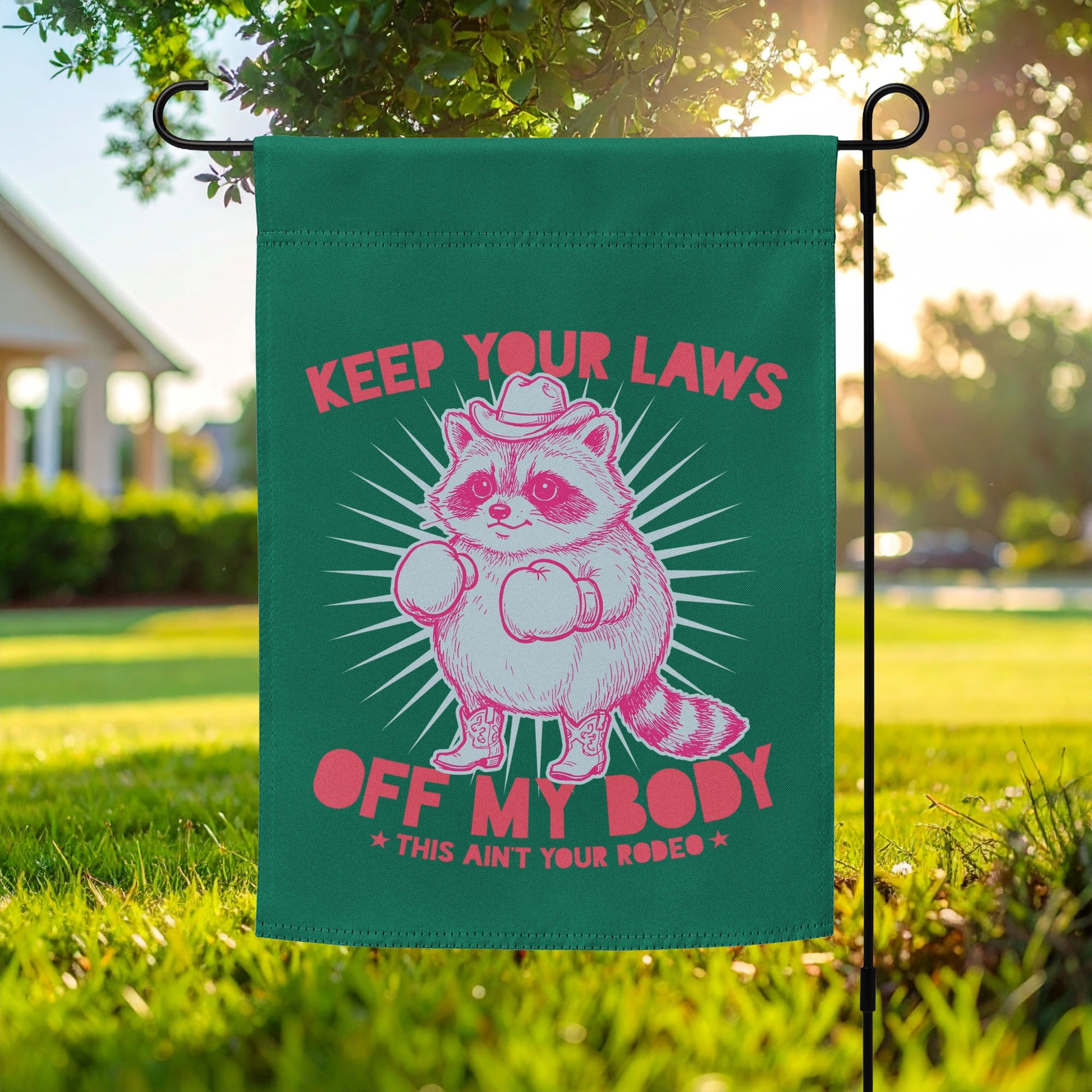 Garden flag featuring pink cowboy raccoon with “Keep Your Laws Off My Body” text on green background, bold feminist protest outdoor decor for reproductive rights.