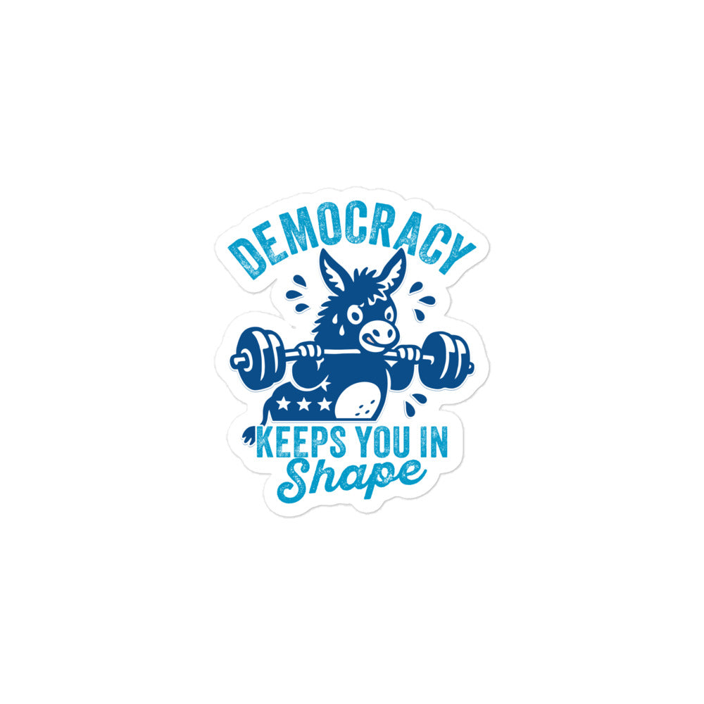 Close-up die-cut sticker of a strong blue donkey holding weights beneath democracy lettering, combining workout humor with civic pride and progressive apparel aesthetics.