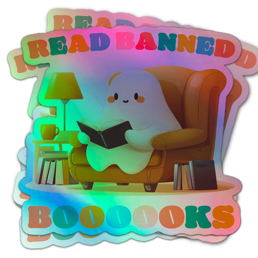 Holographic sticker of a cute ghost sitting in an armchair, reading a book, with the text “Read Banned Boooooks” in colorful letters and stacks of books nearby.