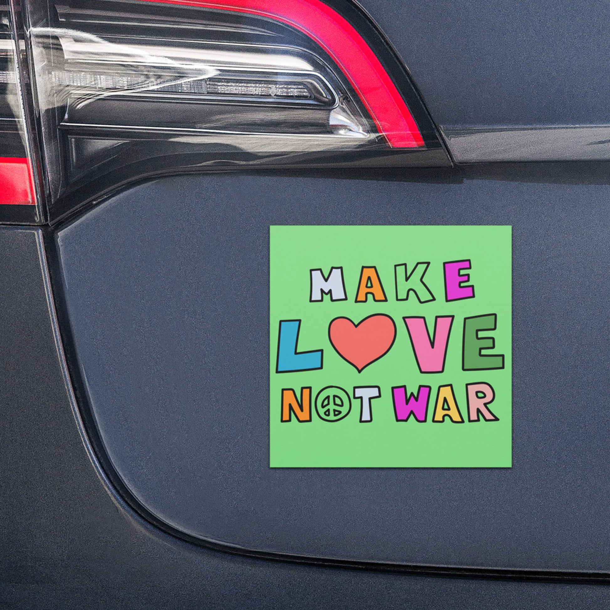 Green car magnet with multicolor “MAKE LOVE NOT WAR” typography and heart symbol displayed on vehicle trunk, playful peace message.