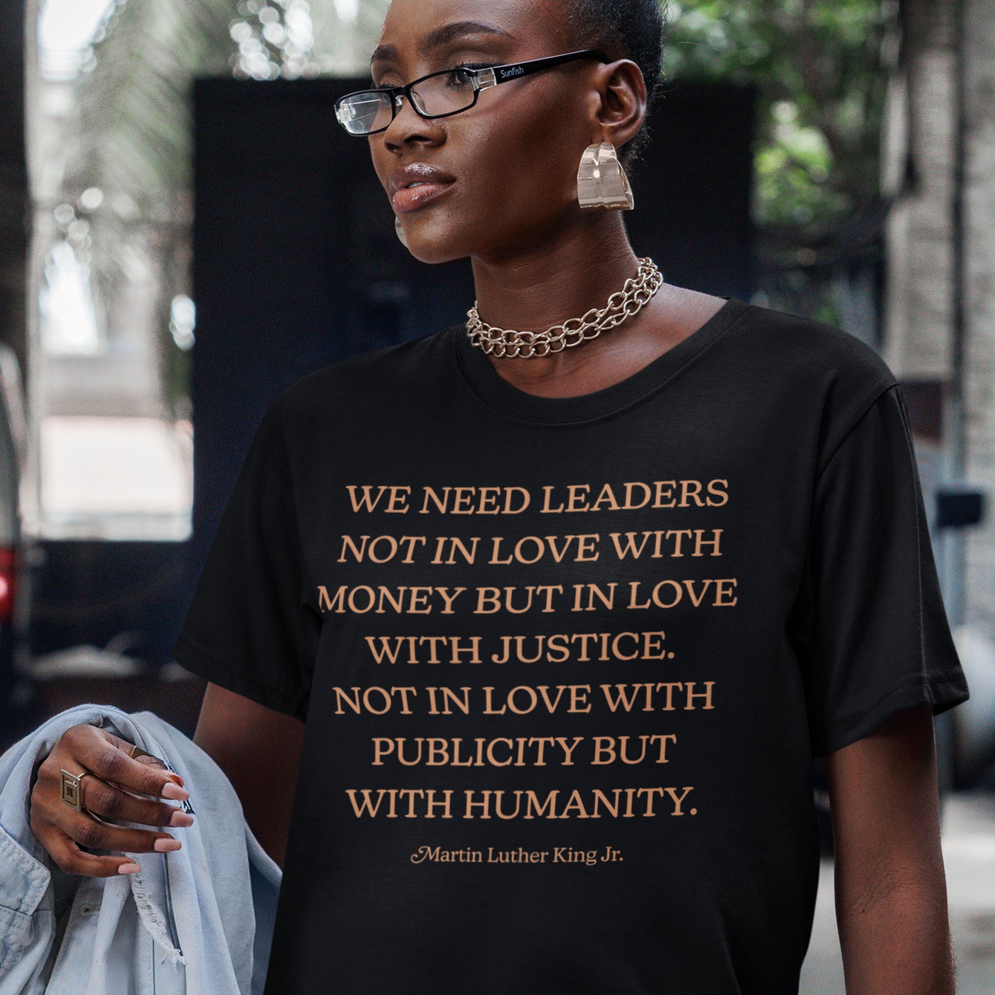A model wearing a black shirt printed with the MLK quote “WE NEED LEADERS NOT IN LOVE WITH MONEY BUT IN LOVE WITH JUSTICE… WITH HUMANITY.” A justice-focused Blue Wave USA design.