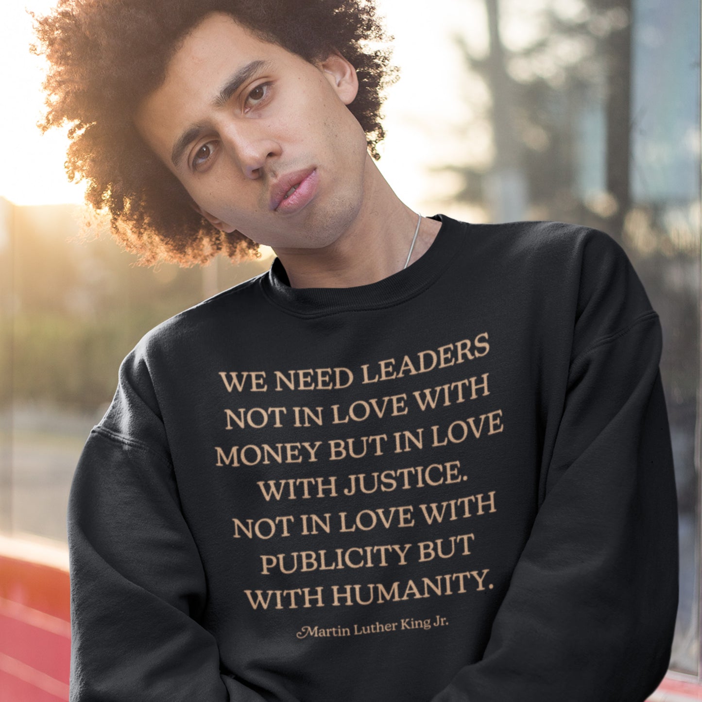 Young man wearing a black sweatshirt featuring the MLK quote: “WE NEED LEADERS NOT IN LOVE WITH MONEY BUT IN LOVE WITH JUSTICE… PUBLICITY BUT WITH HUMANITY.” A powerful civil-rights message.