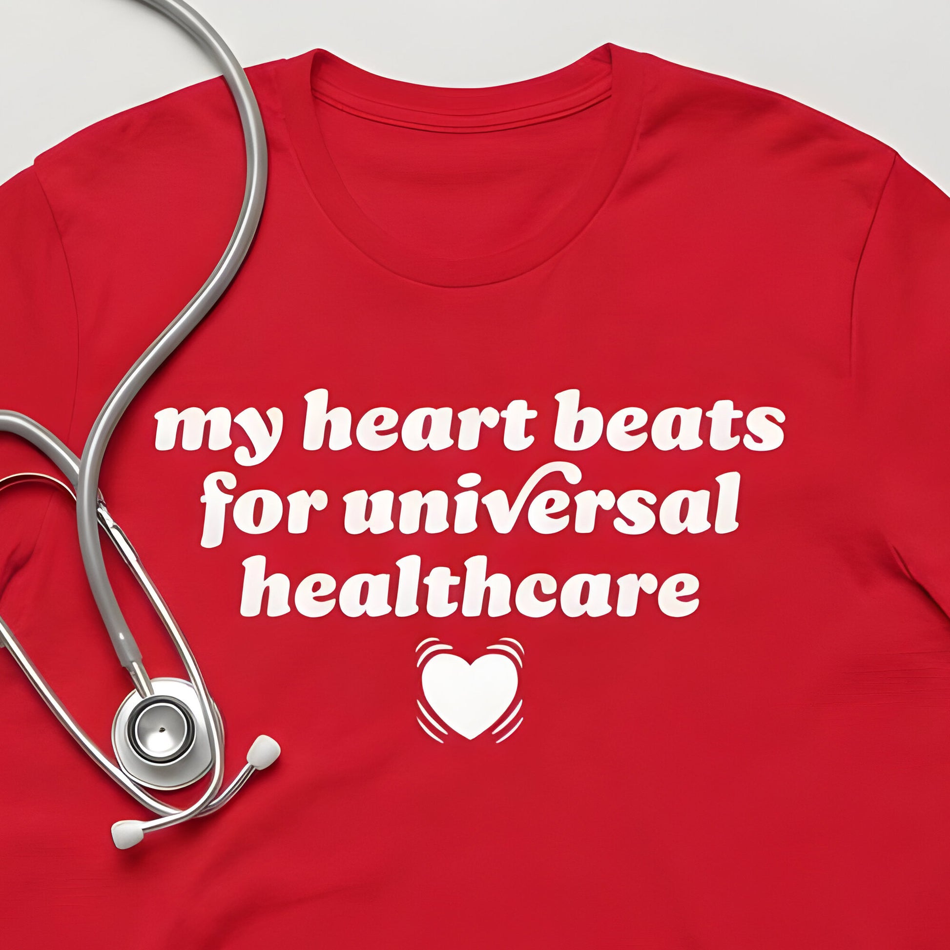 Red unisex t-shirt flat lay featuring stethoscope and bold typography reading “my heart beats for universal healthcare,” a clean healthcare solidarity graphic and justice-focused design.