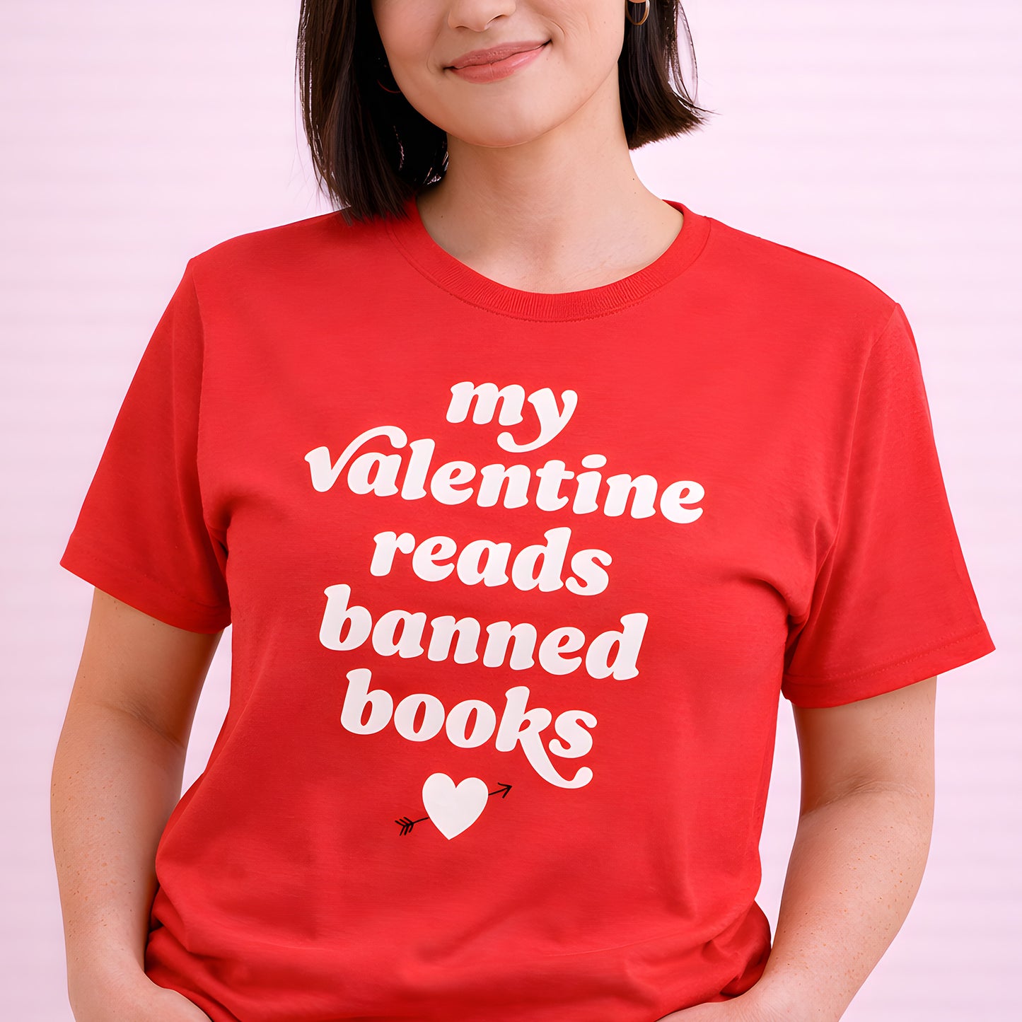 Unisex t-shirt worn by a smiling person, featuring bold retro lettering reading “my valentine reads banned books” with small heart graphic; progressive apparel by Blue Wave USA.