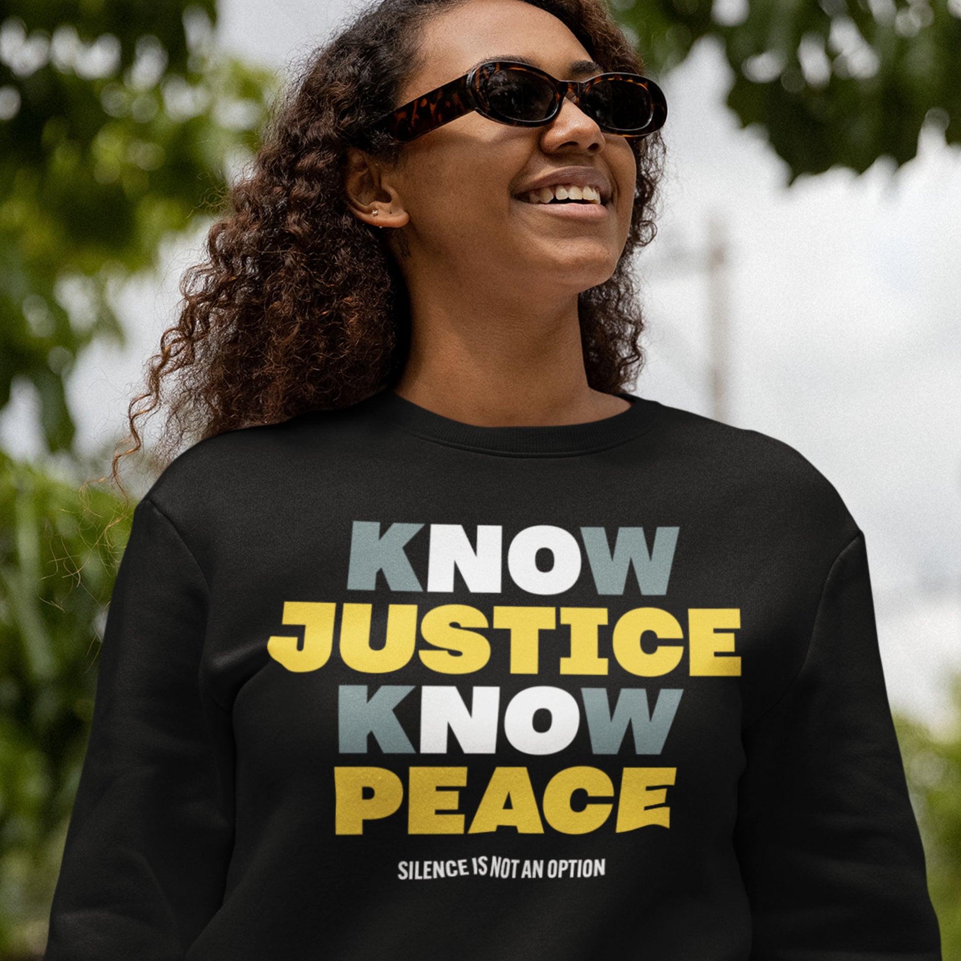 Smiling person wearing a black No Justice No Peace sweatshirt — showing activism and everyday style coming together. Designed by Blue Wave USA for those who lead with conscience.