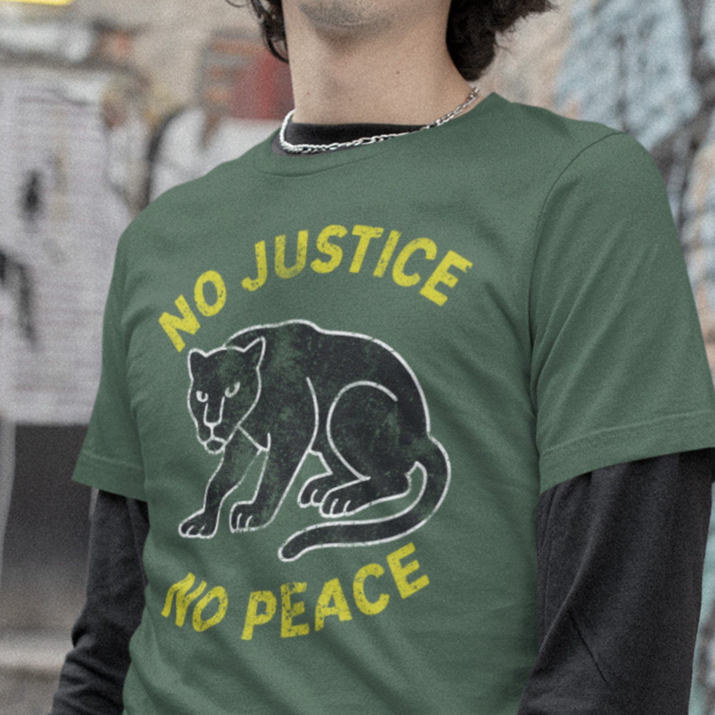 Model wearing green unisex t-shirt printed with “NO JUSTICE NO PEACE” and a distressed panther illustration. Justice-driven activist apparel.