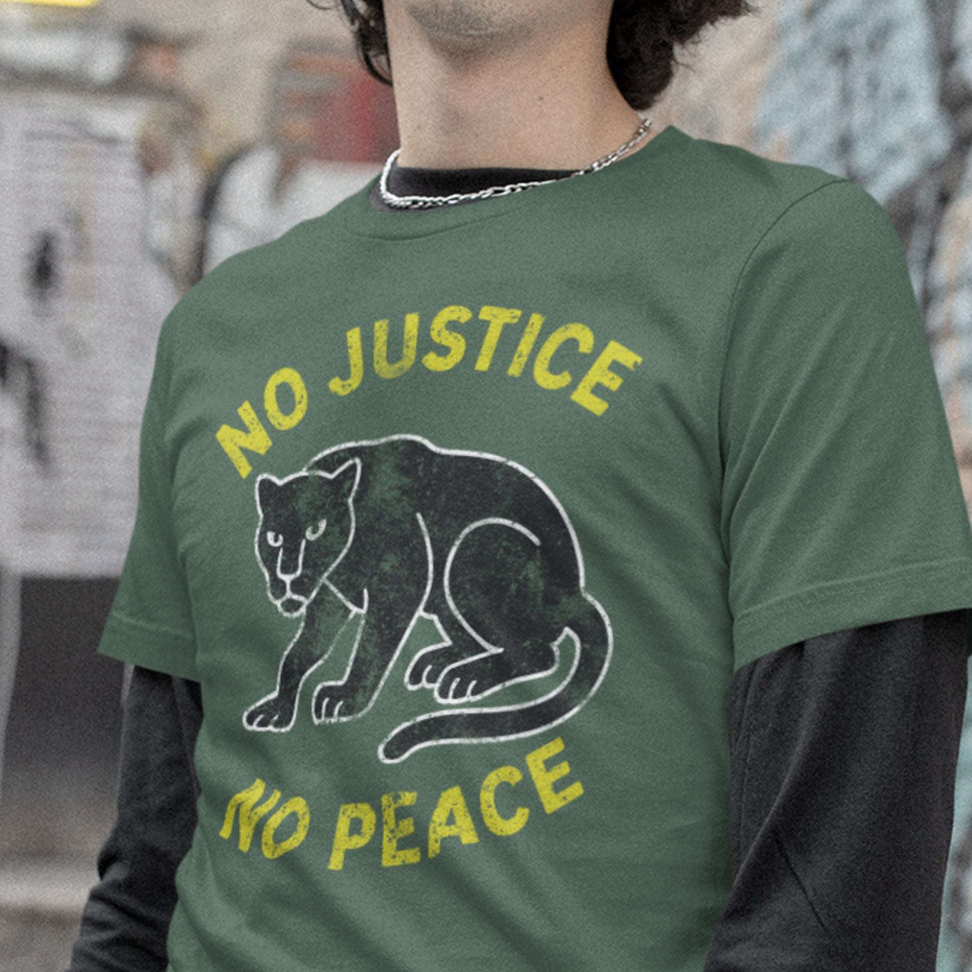 Model wearing green unisex t-shirt printed with “NO JUSTICE NO PEACE” and a distressed panther illustration. Justice-driven activist apparel.