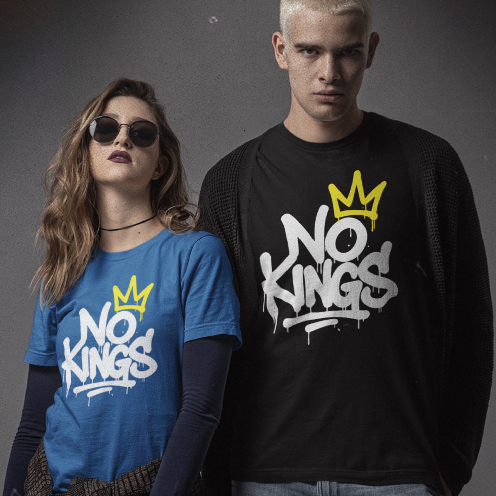 Two models wearing the “No Kings” graffiti t-shirt, one in blue and one in black, standing confidently side by side in urban lighting.